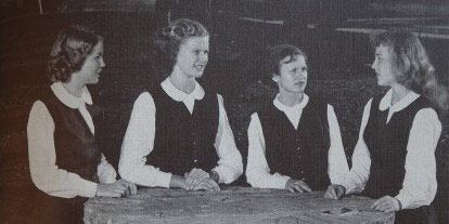 A group of girls are sitting around a table in a black and white photo.