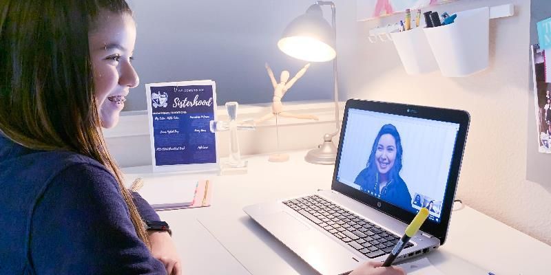 A girl is sitting at a desk using a laptop computer.