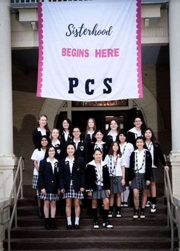 A group of girls are standing in front of a sign that says sisterhood begins here pcs