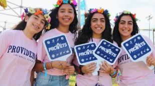 A group of young women wearing pink shirts and flower crowns are holding signs.