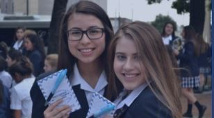 Two girls in school uniforms are standing next to each other and smiling.
