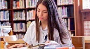 A woman is sitting at a table in a library reading a book.