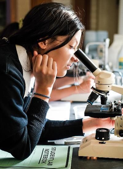 A girl is looking through a microscope in a science lab