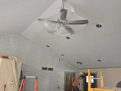 Ceiling being painted, a ceiling fan and other items are protected with plastic.