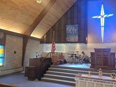 Interior of a church with a stage, cross, and drums. A person is sitting at the drums.