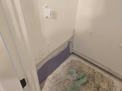 Interior corner with exposed drywall, unfinished floor, and electrical outlet.