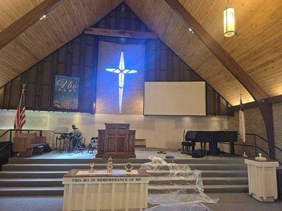 Interior of a church sanctuary, featuring an illuminated cross, pulpit, piano, and stage.