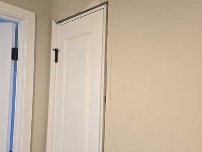 White door, partially open, with dark hinges and trim against a beige wall.