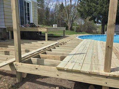 Deck under construction with framing and partially laid planks next to a swimming pool.