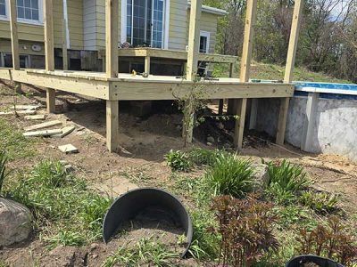 A deck under construction next to a house with a small above-ground pool.