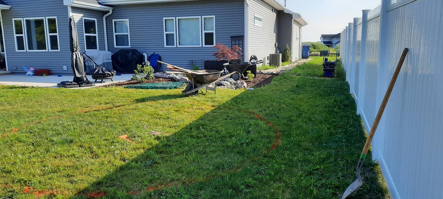 Backyard with a house, green grass, a white fence, and landscaping work in progress.