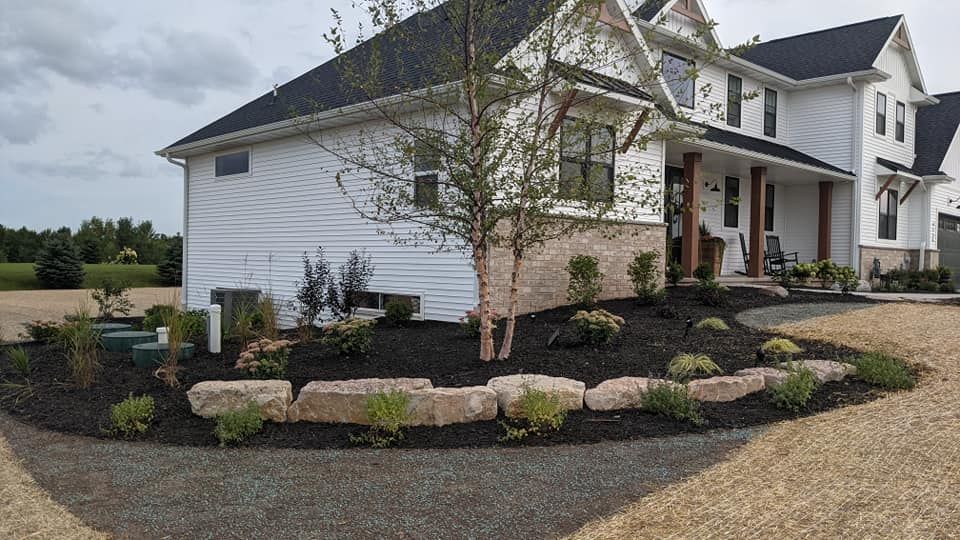 White house with dark roof and gravel driveway, surrounded by landscaping and rock border.