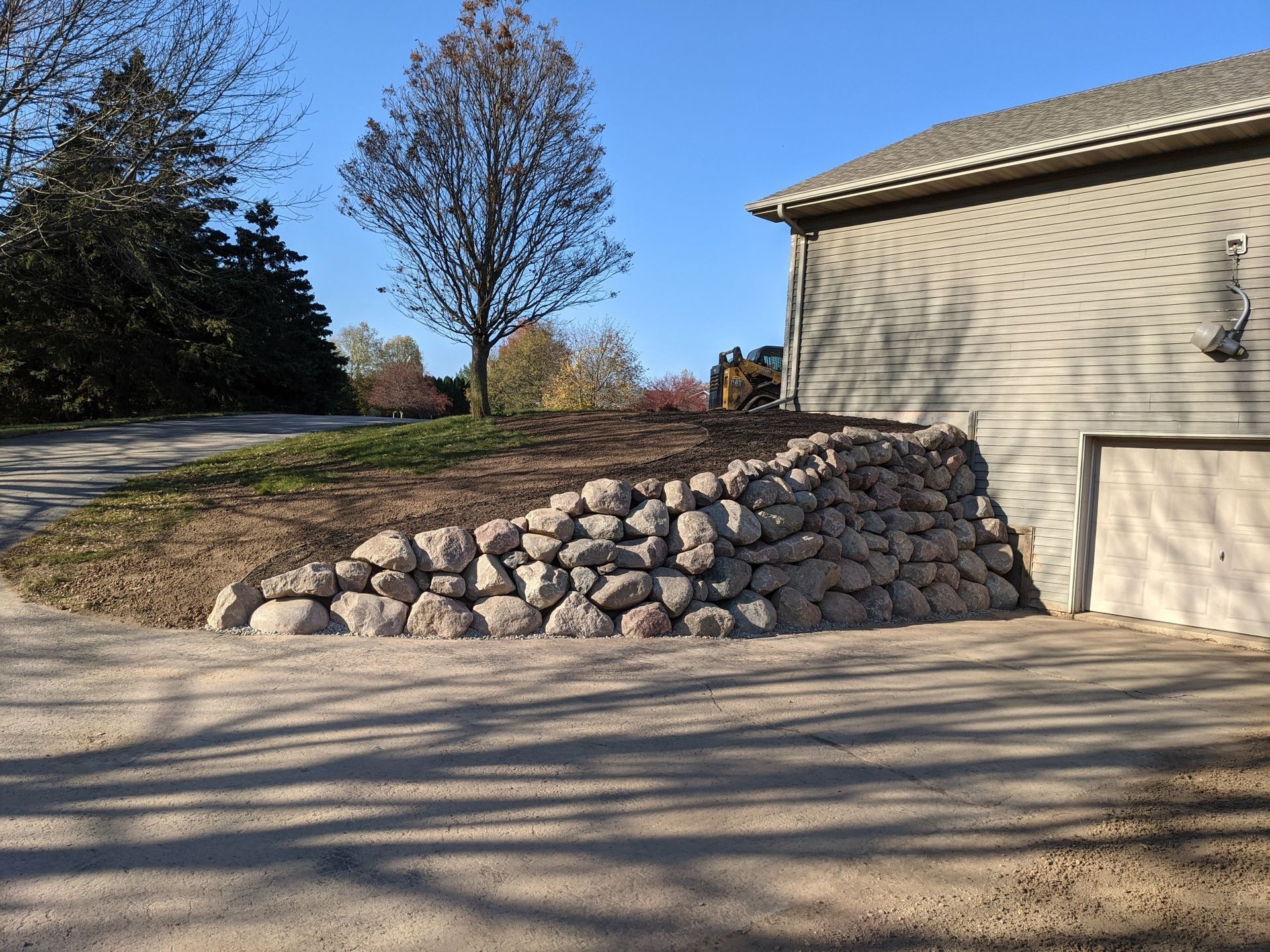 Rock wall next to a beige building and driveway on a sunny day.