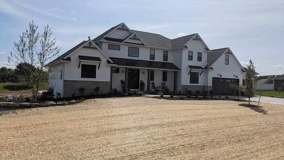 White two-story house with black roof, brick facade, and open front yard with dry grass.