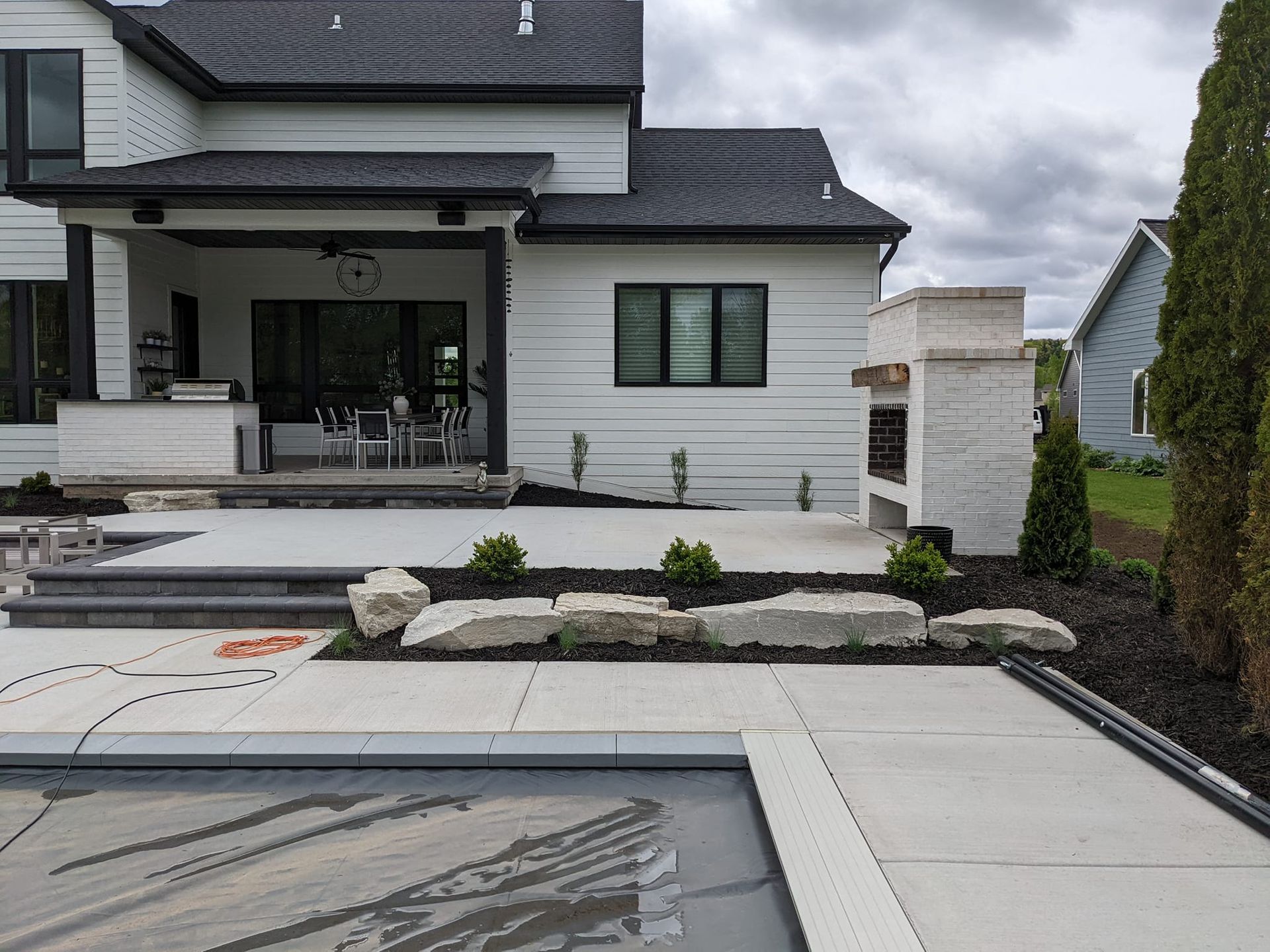Backyard with house, pool, patio, and outdoor fireplace; overcast sky.