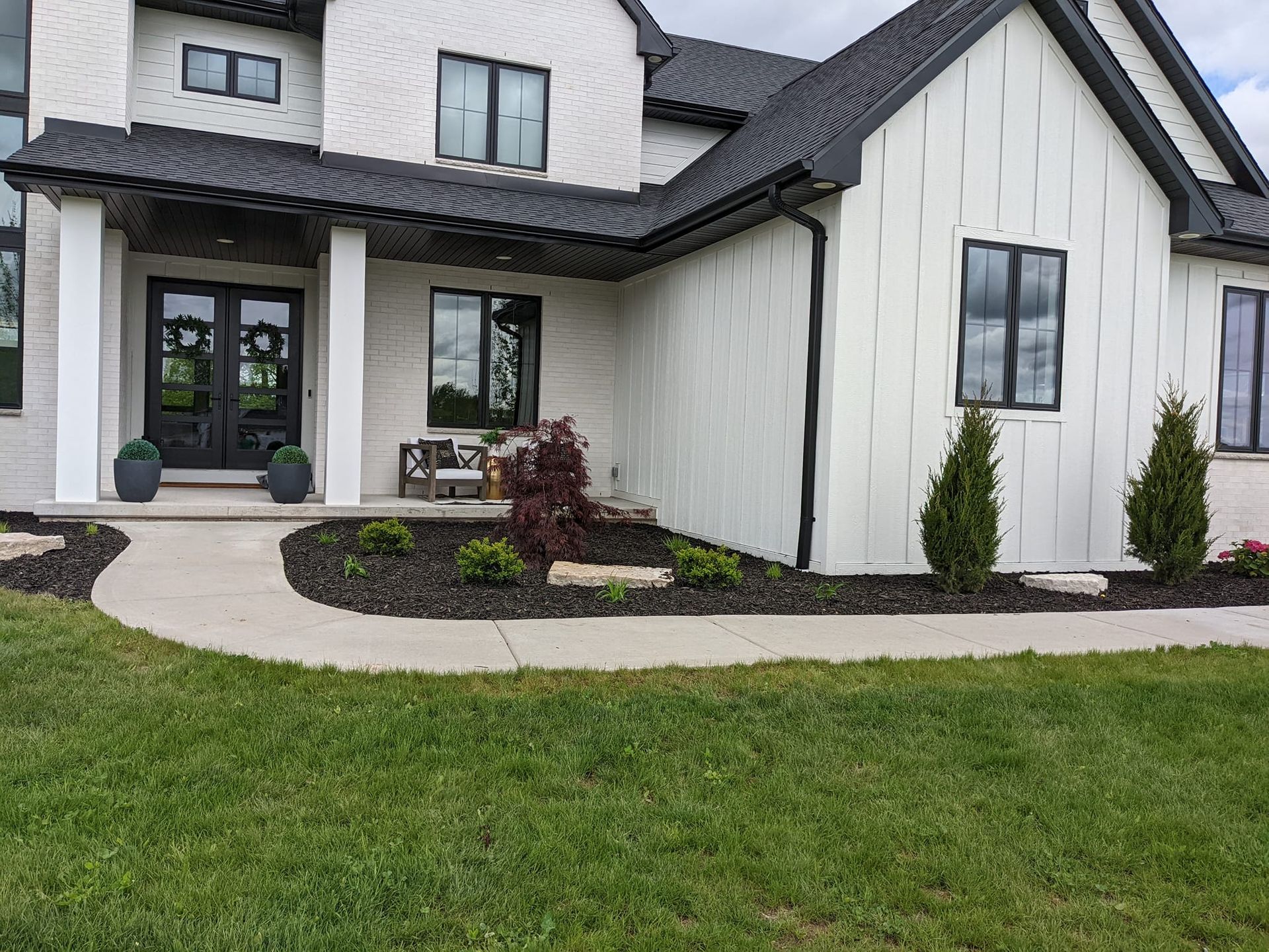 White house with black trim, walkway, and landscaped front yard with green lawn.