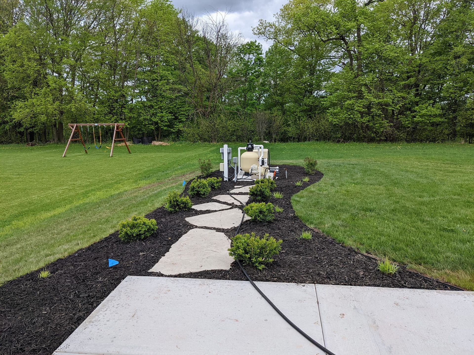 A stone path through a landscaped garden leads to equipment in a backyard.