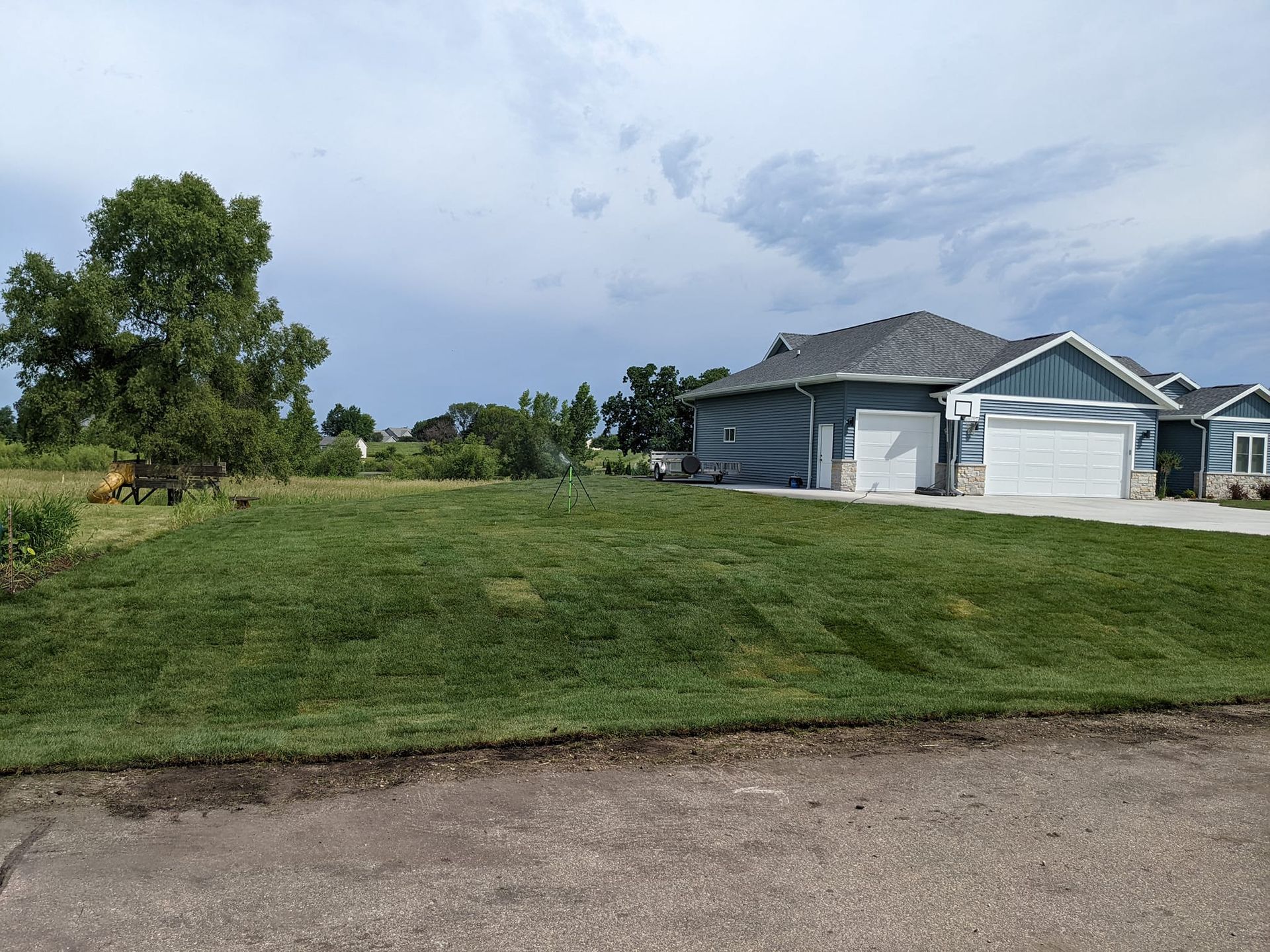 Newly sodded lawn in front of a partially constructed house with a blue facade under a cloudy sky.
