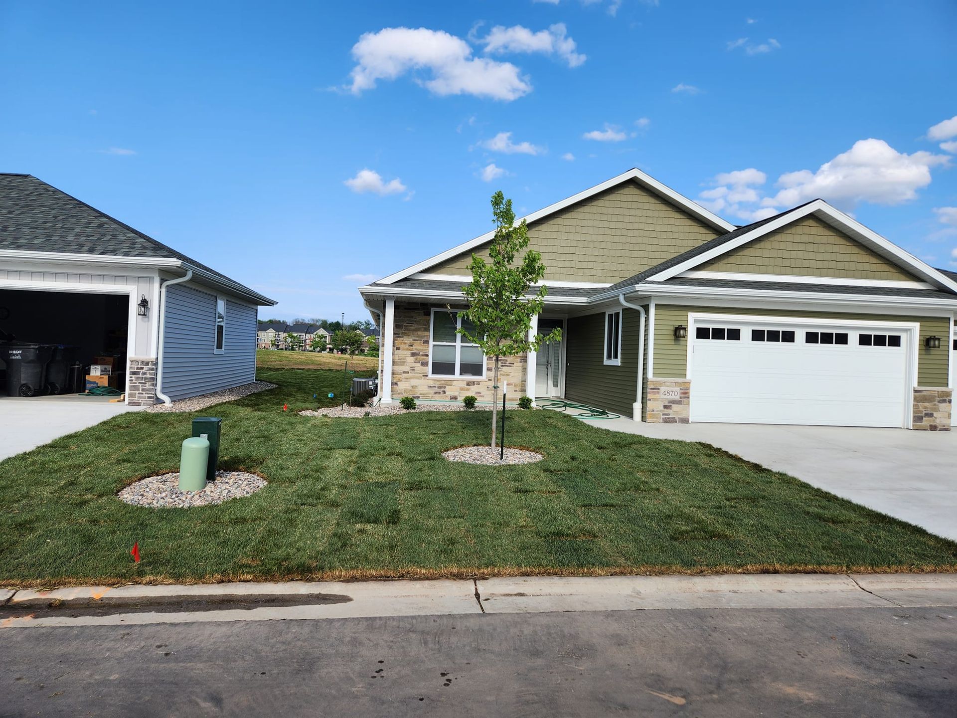 Two-car garage home with green siding and a white garage door, next to a matching garage. Blue sky.