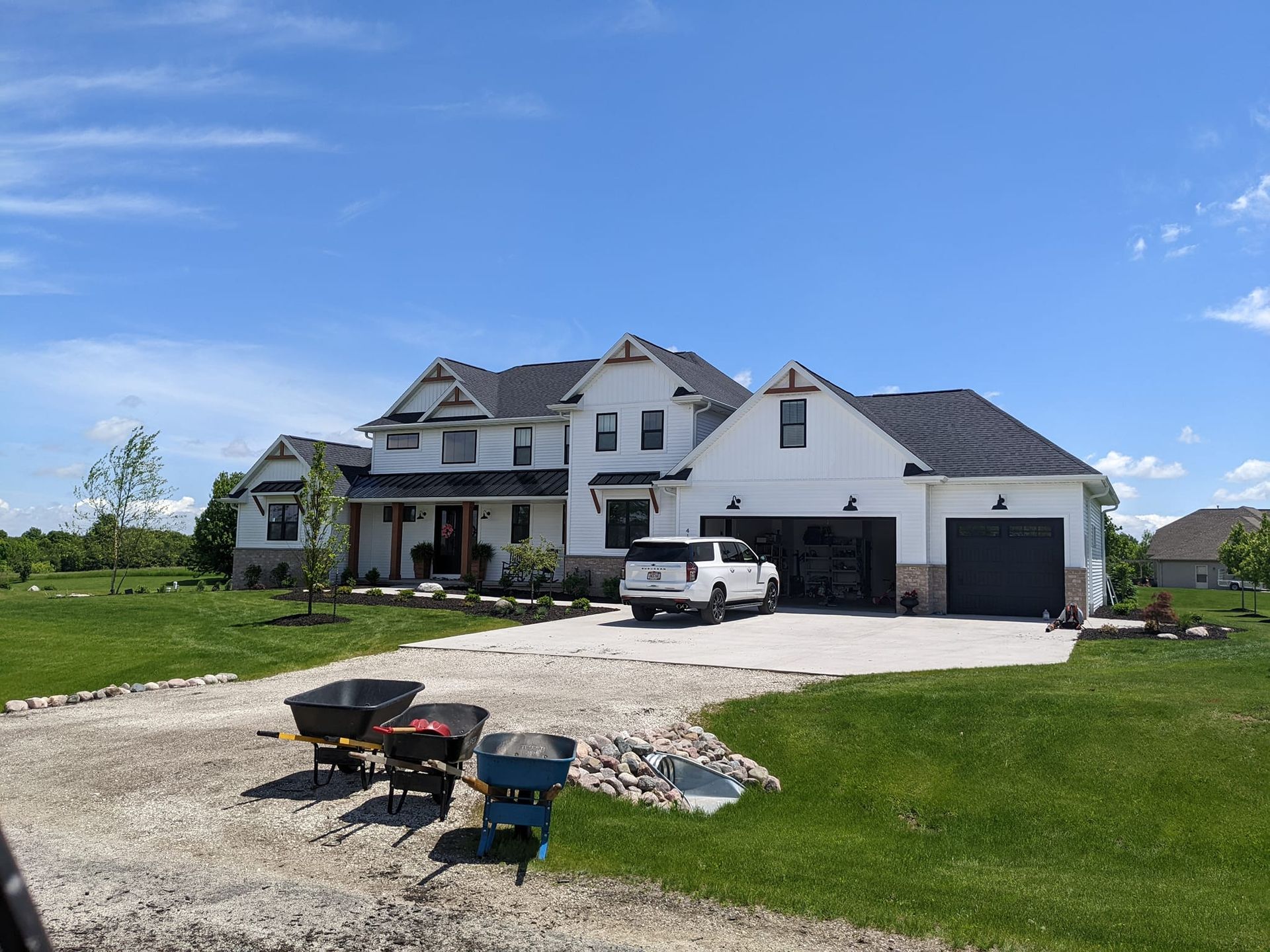 White house with black roof, attached garage, gravel driveway, and a white pickup truck on a sunny day.