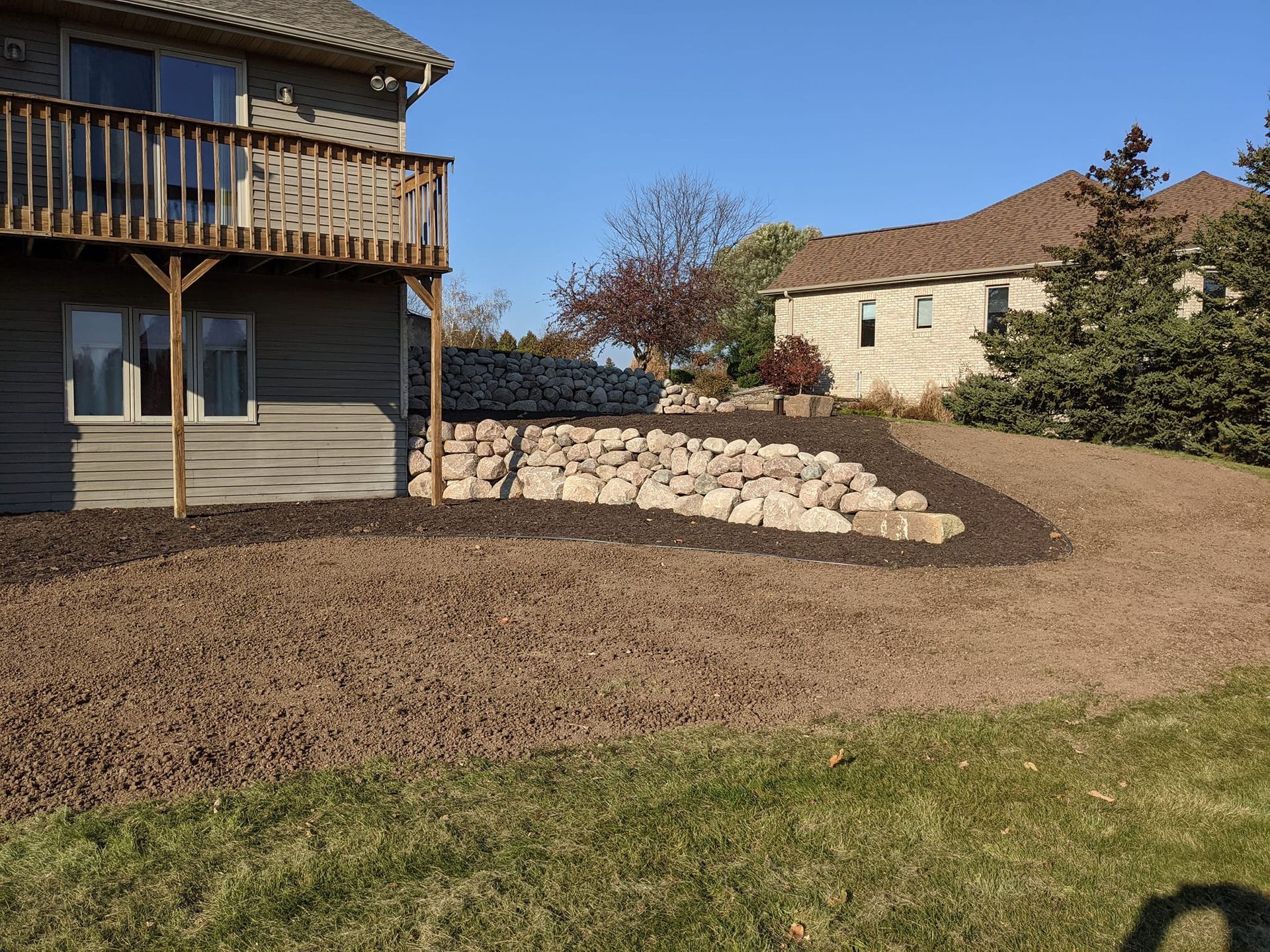 A house with a wooden deck, a rock retaining wall, and brown mulch in the yard.