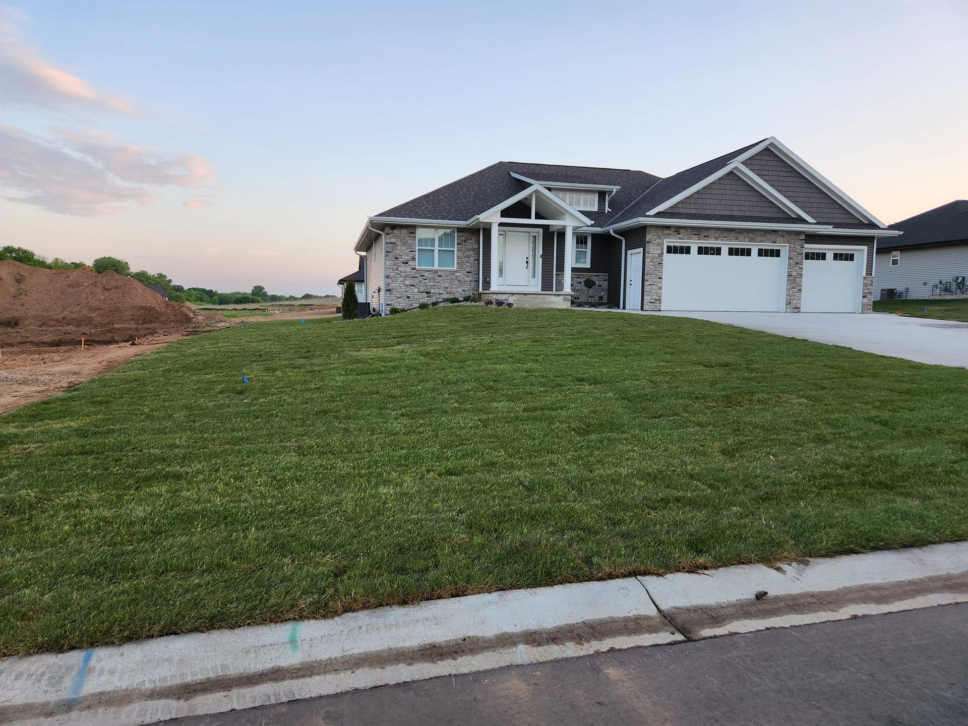 House with gray and blue siding, two-car garage, and green lawn under a blue sky.