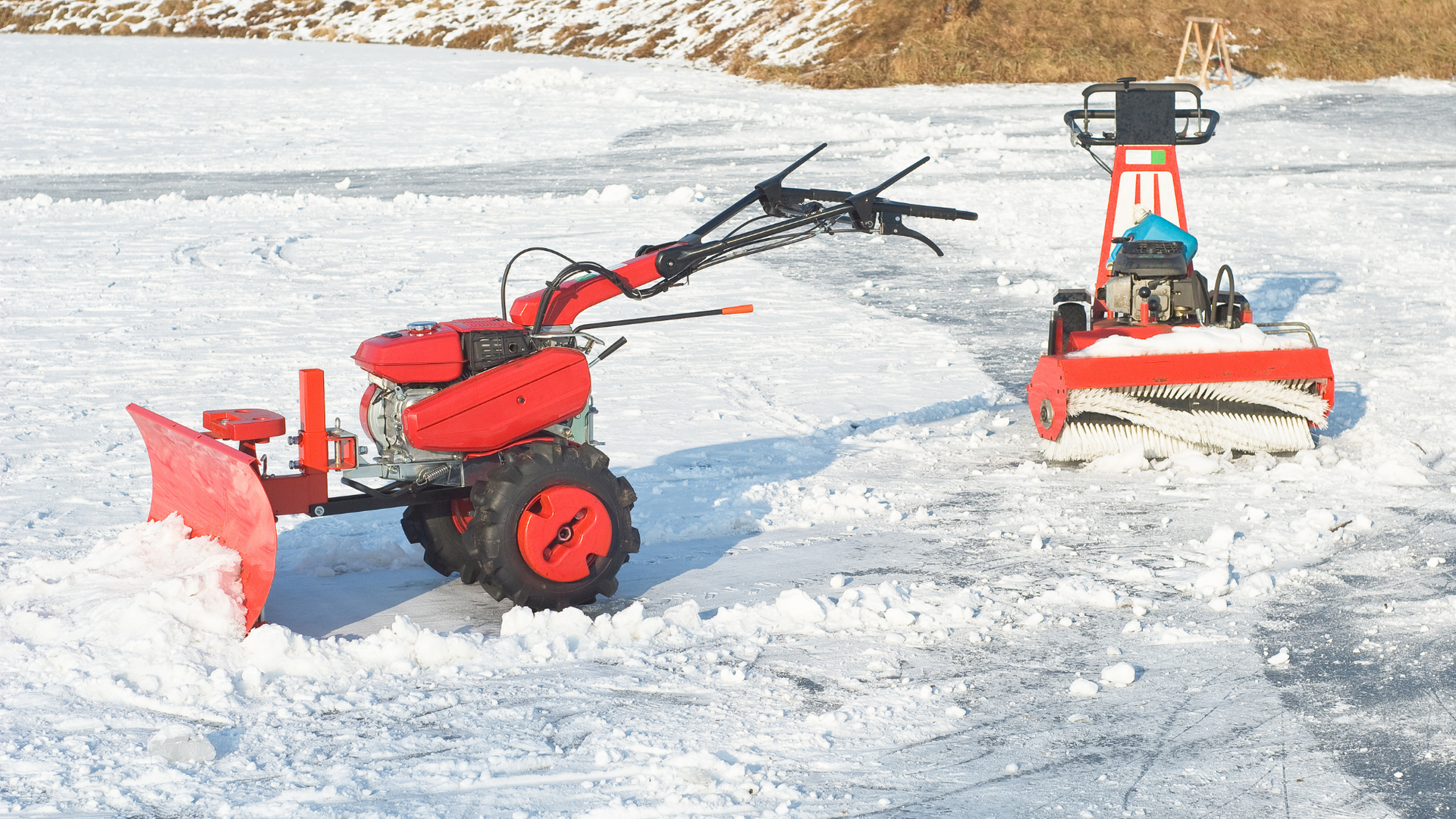 Two red snow removal machines clearing snow on a frozen lake.