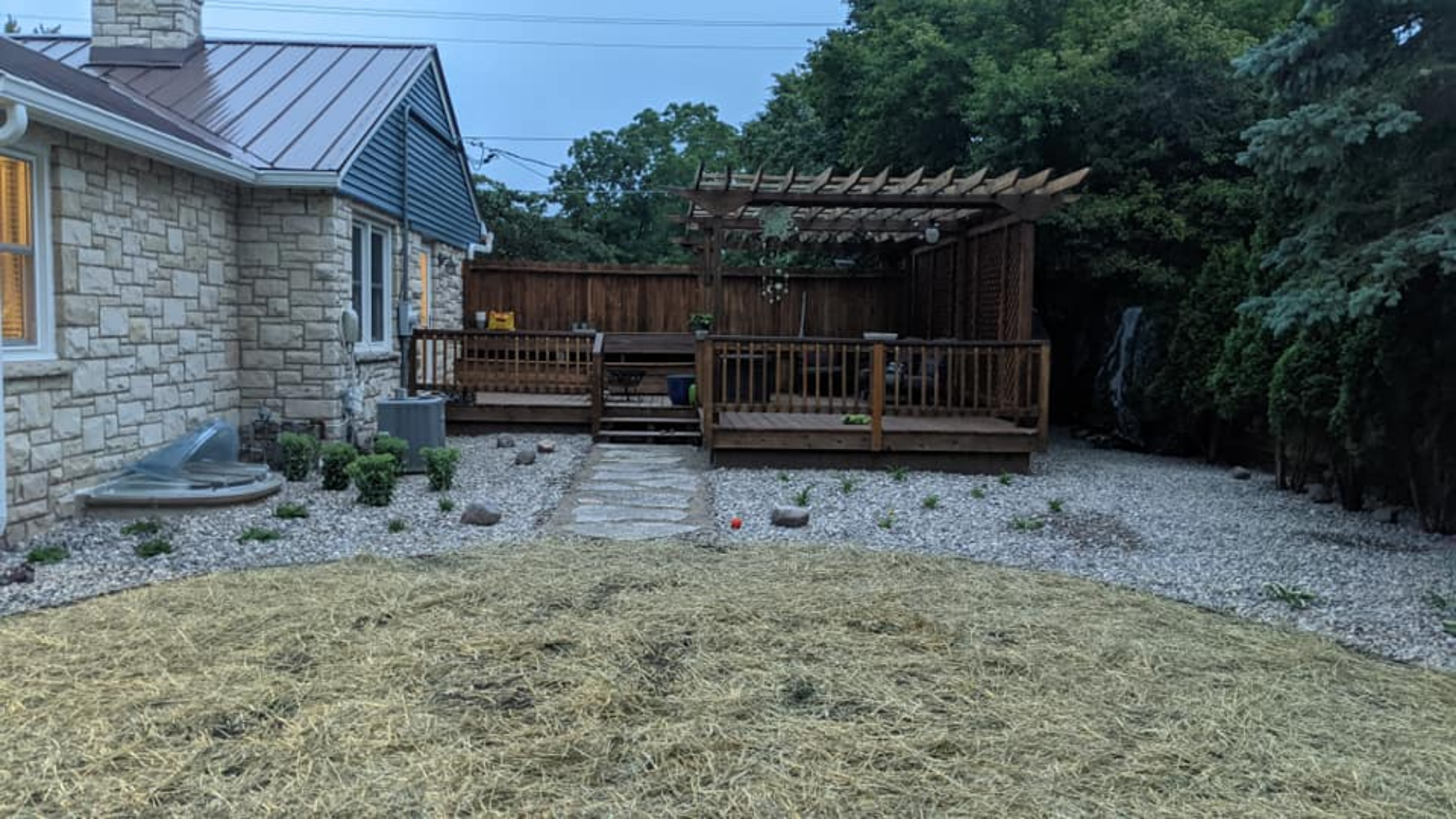 Backyard deck with pergola, stone house, and gravel landscaping.