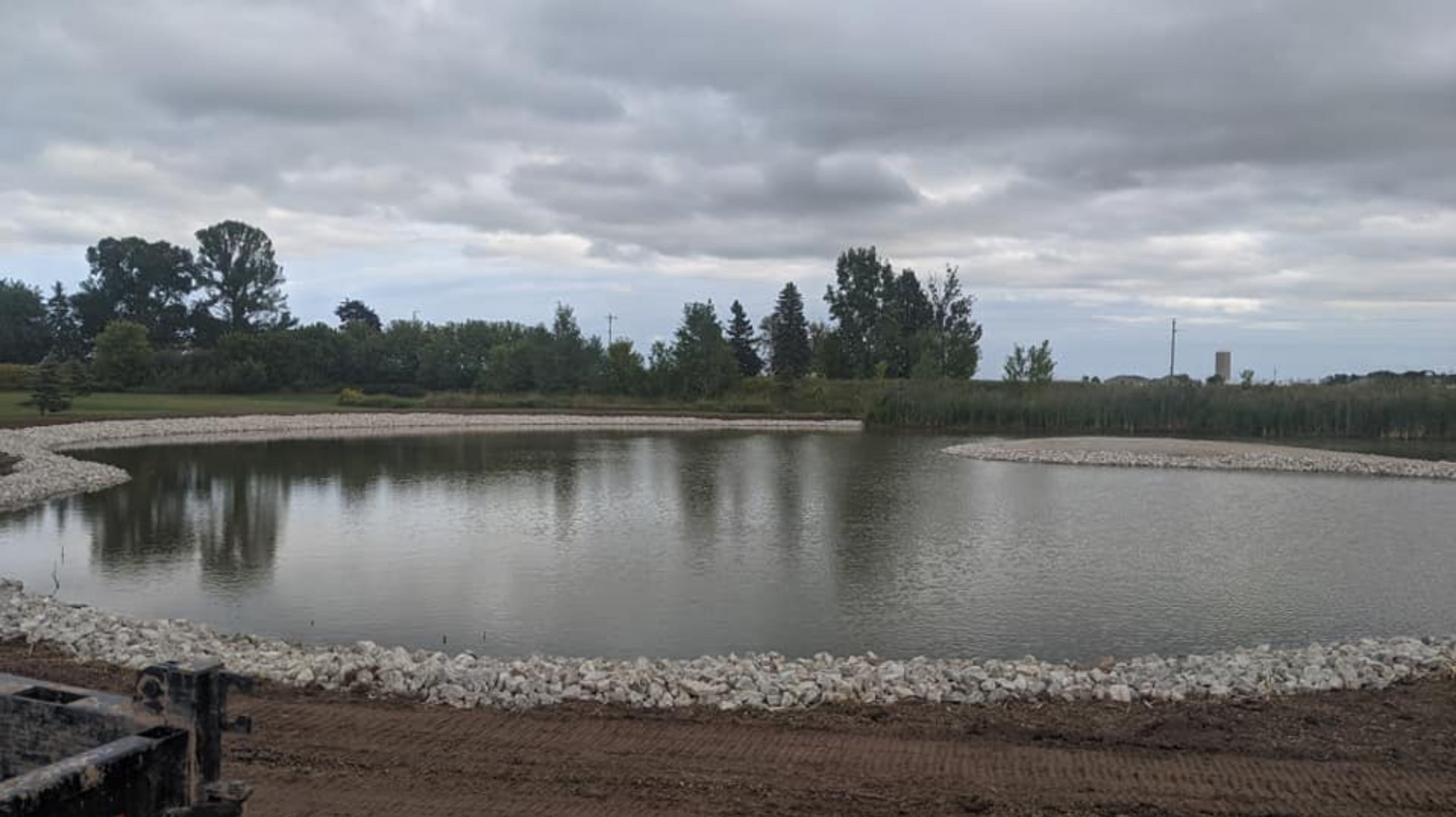 A pond with a rock border on a cloudy day. Trees are visible in the background.