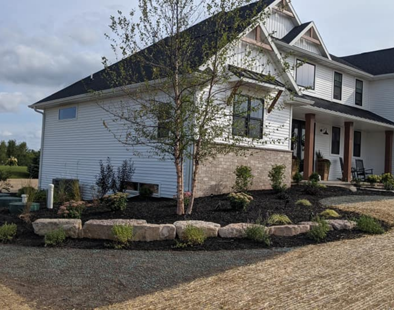 White house with black roof, brick and stone accents, surrounded by landscaping with rocks and mulch.