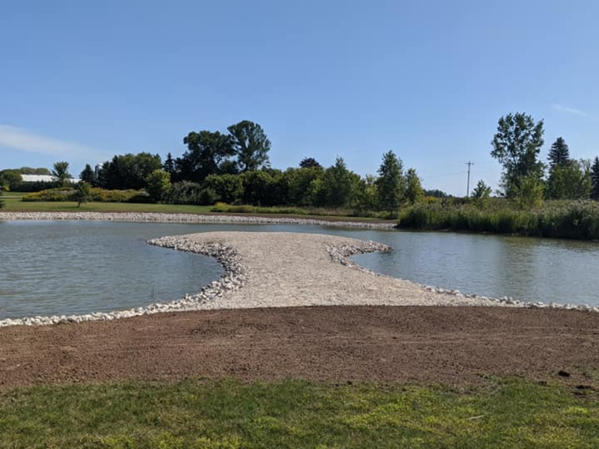 A pond with a gravel pathway extending into the water on a sunny day.