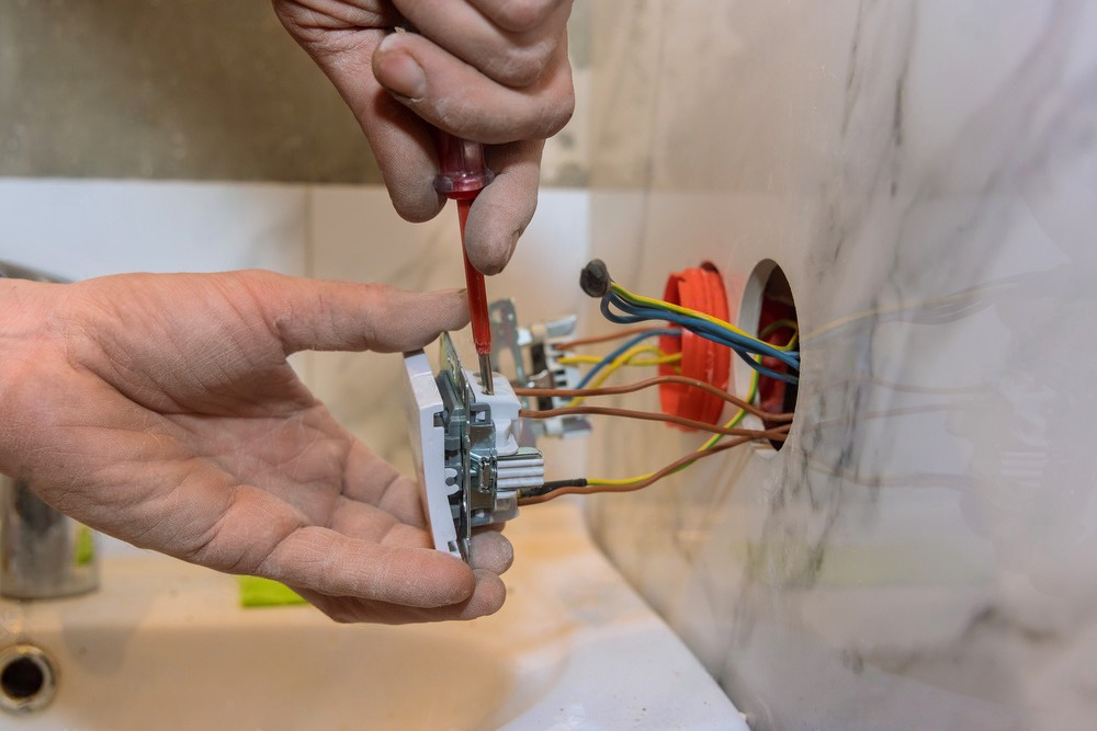 a person is fixing a light switch with a screwdriver .