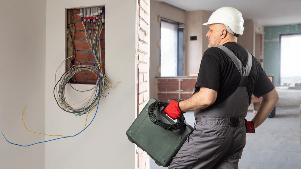 a man is holding a tool bag in front of a wall with wires hanging from it .