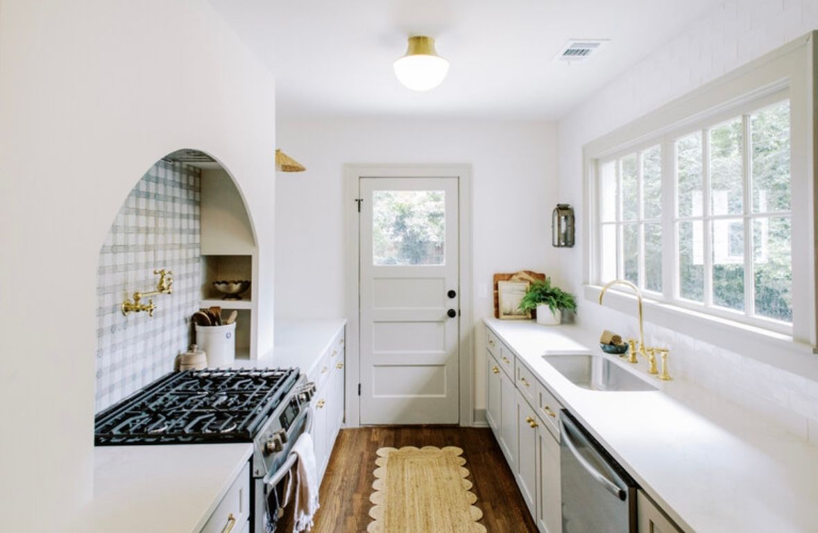 A kitchen with white cabinets , a stove , a sink and a window.