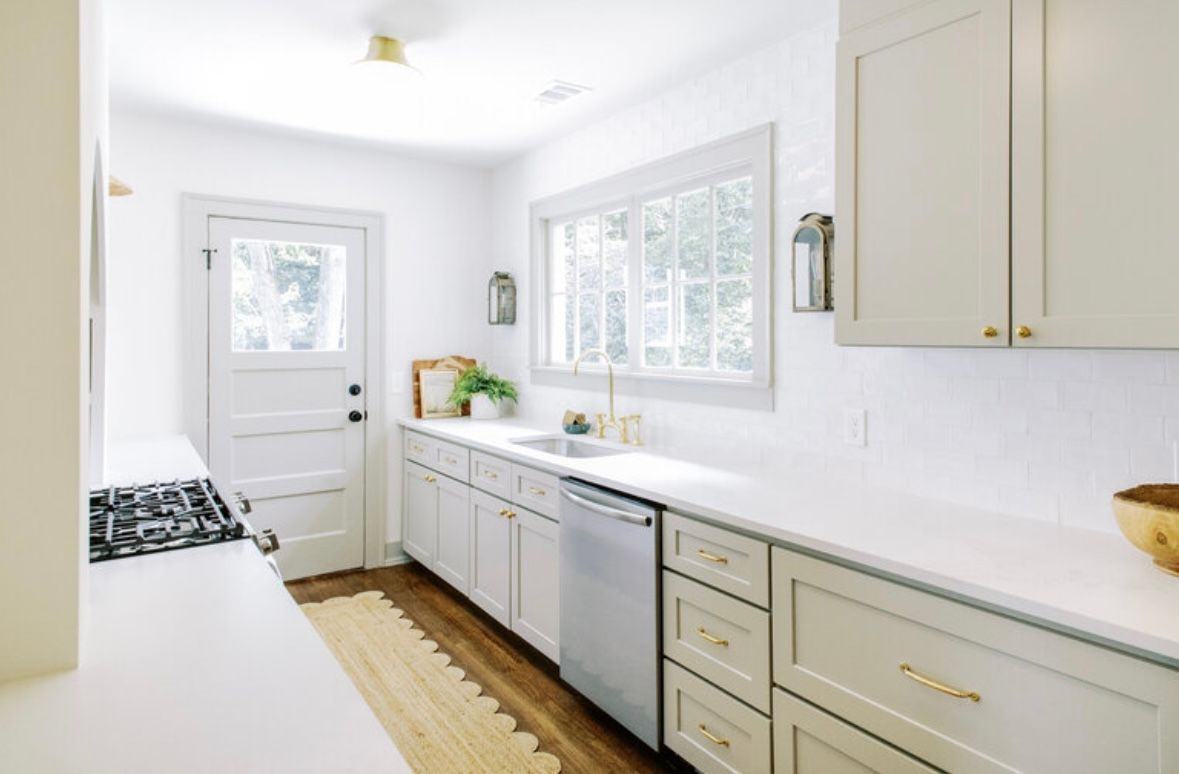 A kitchen with white cabinets , a stove , a sink , and a window.