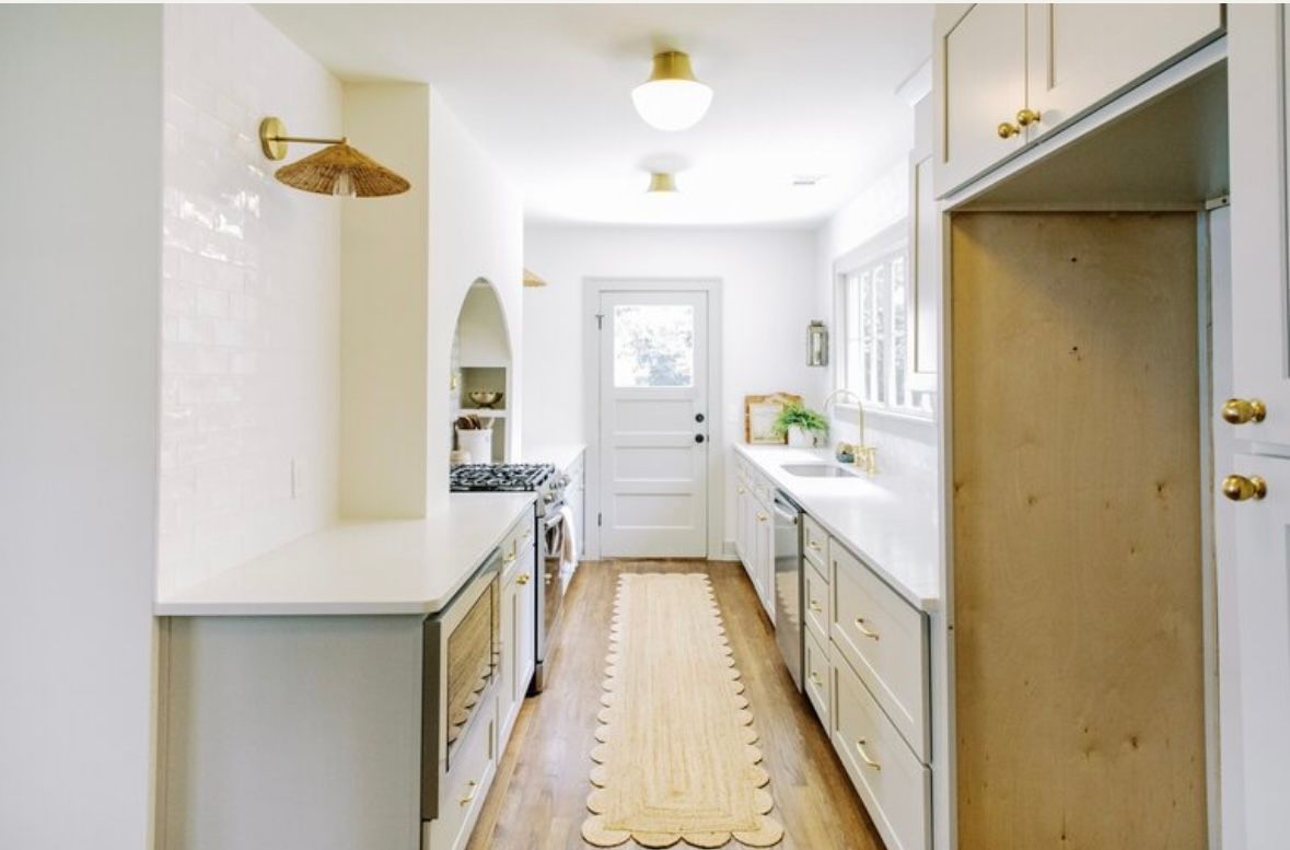 A long hallway in a kitchen with white cabinets and wooden floors.