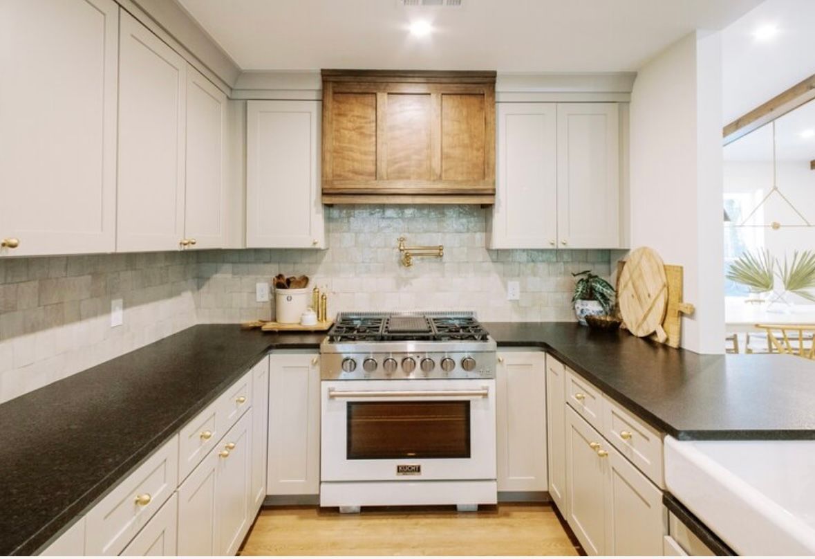 A kitchen with white cabinets , black counter tops , a stove and a sink.