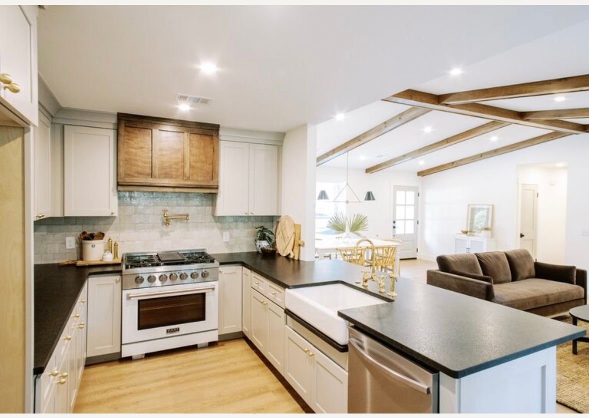 A kitchen with white cabinets , a stove , a sink , and a couch.