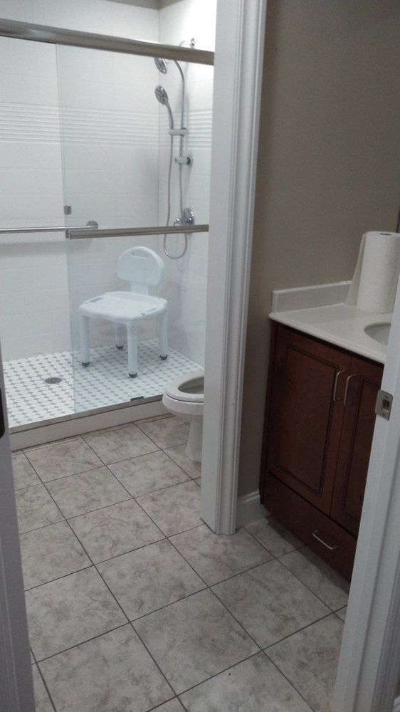 A bathroom with a toilet , sink , shower and chair.