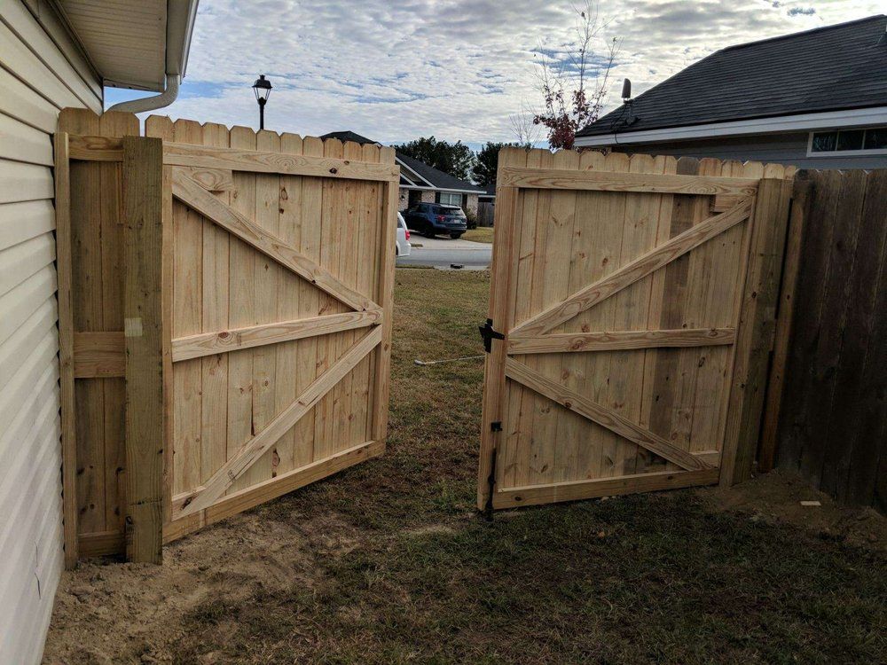 A wooden gate is open in a yard next to a house.