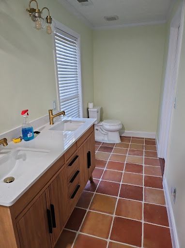 A bathroom with two sinks , a toilet and a window.