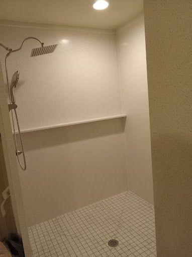 A shower with a shower head and a shelf in a bathroom.