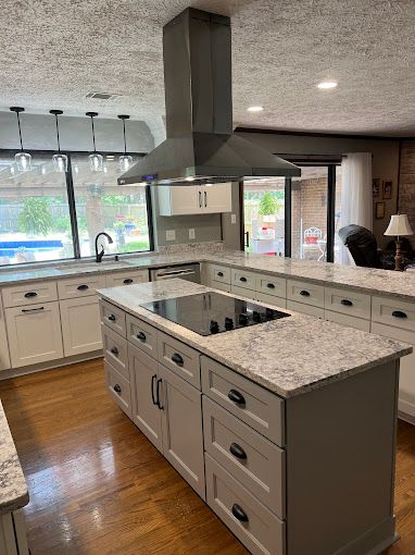 A kitchen with white cabinets and a large island with a stove top oven.