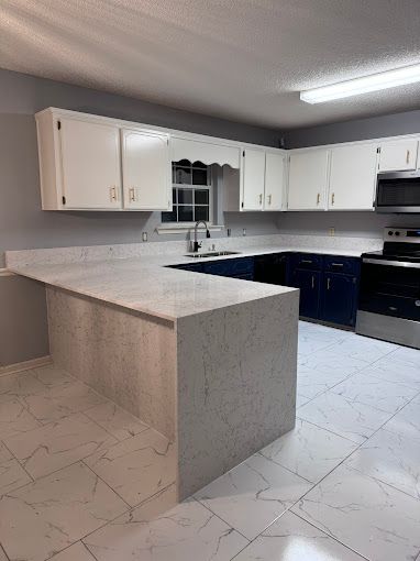 A kitchen with white cabinets , blue cabinets , a stove , microwave and sink.