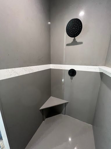 A shower with a black shower head and a corner seat.