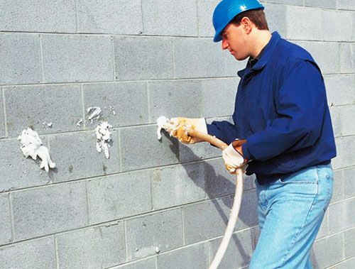 Worker in blue uniform using a hose to clean a gray cinderblock wall