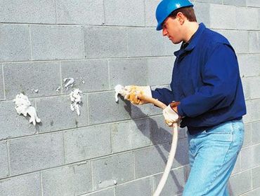 Worker in blue uniform using a hose to clean a gray cinderblock wall