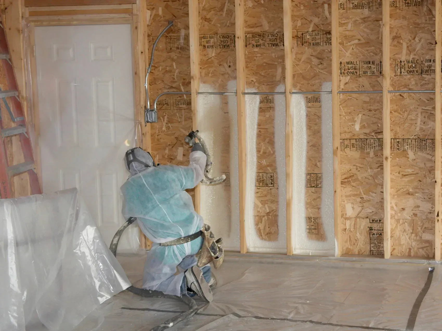Worker spraying insulation foam inside a framed wall in a renovation site