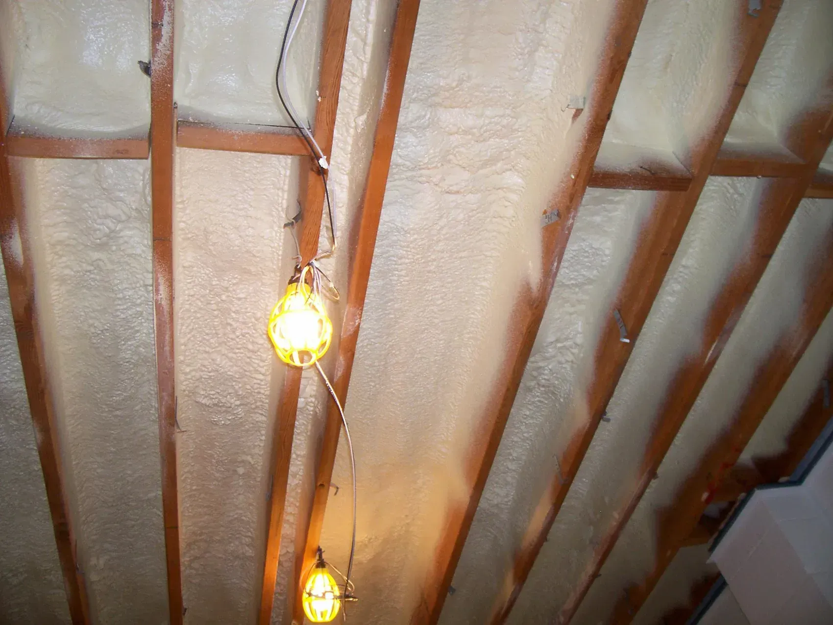 Two hanging light bulbs under a wooden ceiling with white insulation panels
