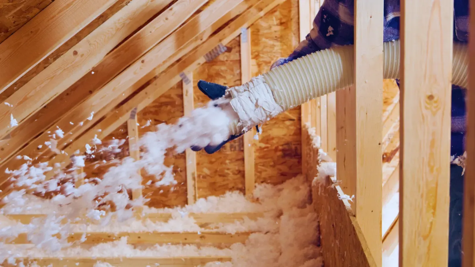 Person blowing loose insulation from an attic through a flexible hose during home insulation work